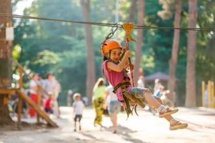 Happy school girl enjoying activity in a climbing adventure park on a summer day